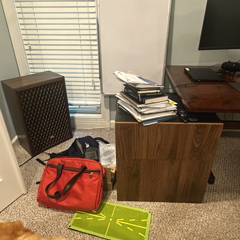 The same home office before organizing, with stacked paperwork and bags on the floor